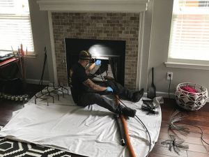 fireplace-chimney-cleaning Texas Air Duct Cleaning tech sitting on the ground cleaning a client's chimney.